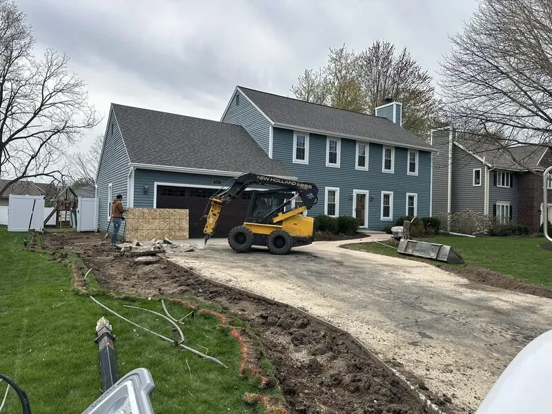 Hydraulic breaker demolishing old concrete driveway at blue colonial home