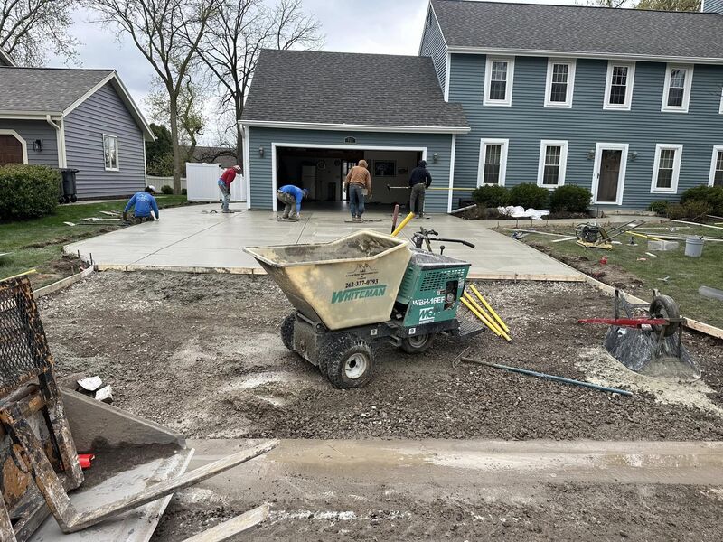 Crew actively pouring and finishing fresh concrete at same blue colonial home