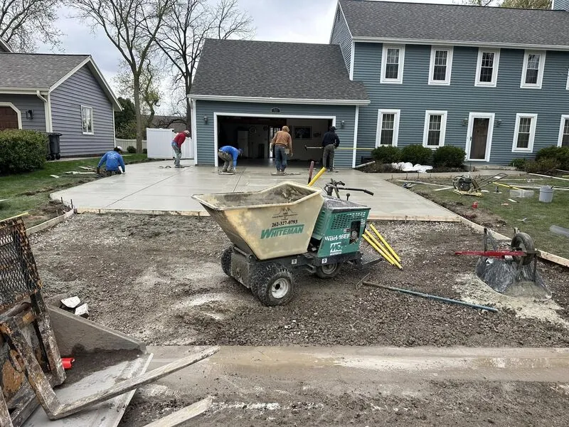 Crew actively pouring and finishing fresh concrete at same blue colonial home