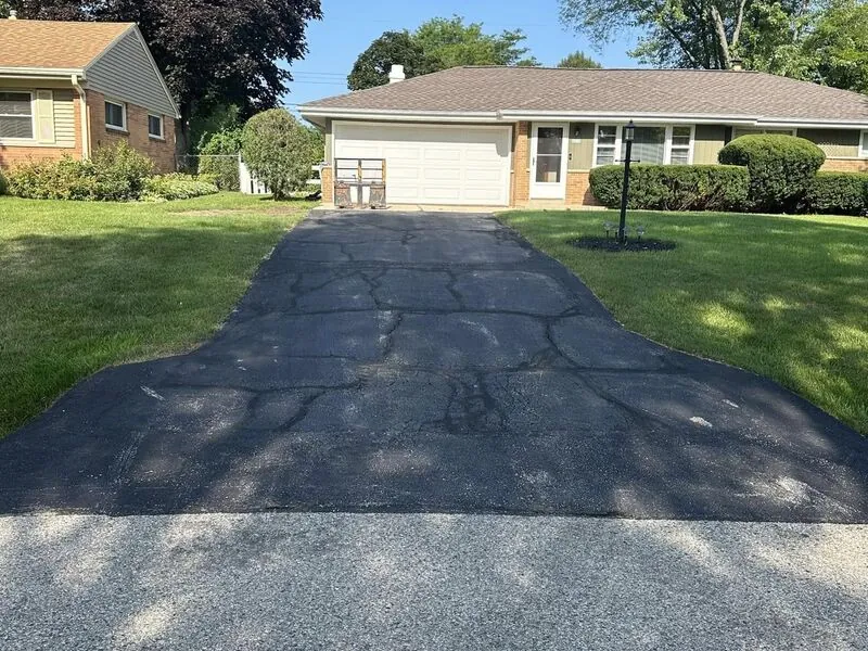 Old cracked asphalt driveway before concrete replacement at brick ranch home
